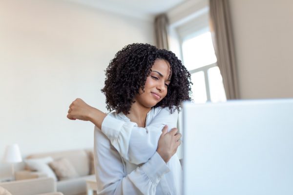 Portrait of young stressed woman touching aching back and shoulder with pained expression, suffering from backache after working on pc