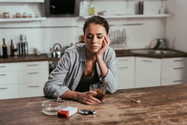 Worried woman showing addiction to alcohol, beside cigarettes and pills
