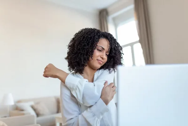 Woman stretching at desk representing pain relief and stress management through ThaoQi acupuncture