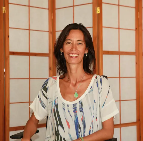 Portrait of Thao, a professional holistic healing practitioner at ThaoQi, smiling in a serene treatment room with a traditional Japanese Shoji screen background